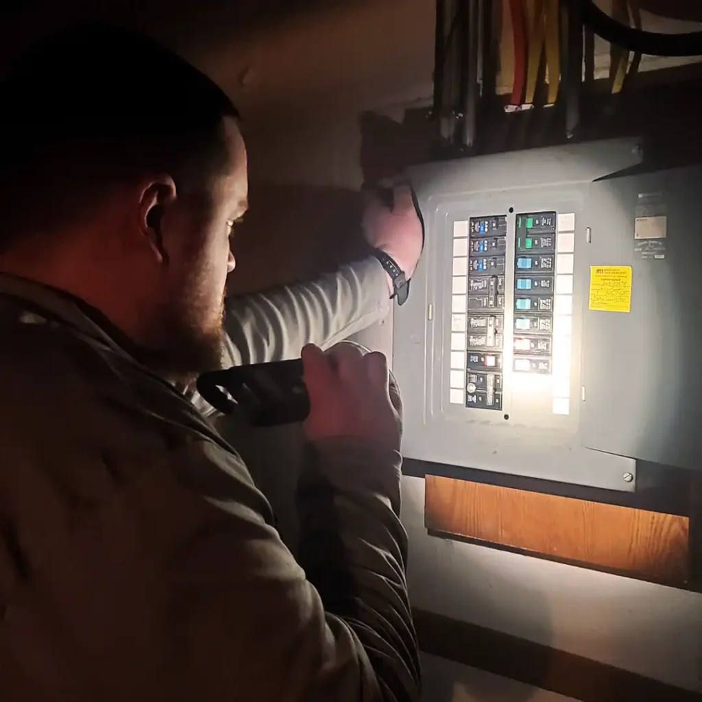 Picture of a home inspector checking an electrical panel with flashlight.